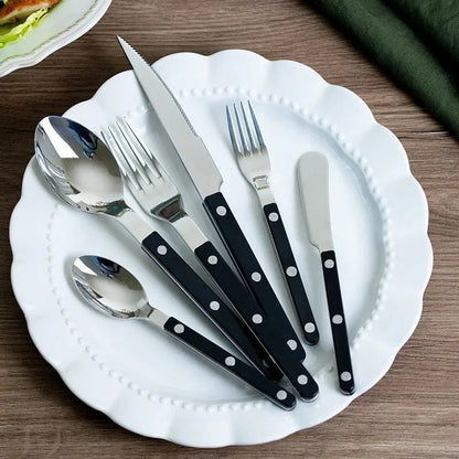 Black handled six piece flatware set on a scalloped white plate on a wooden table