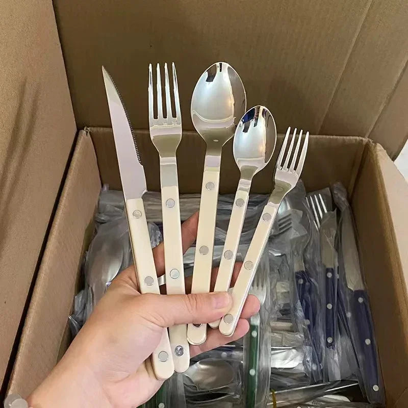 Beige handled flatware pieces held in a hand over a cardboard carton of bagged flatware
