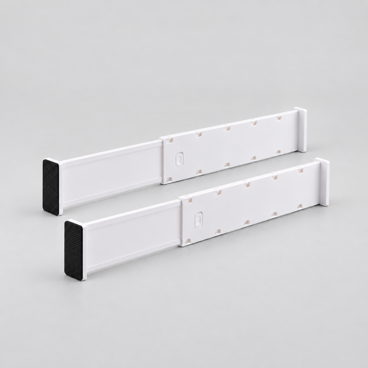 Two long white expandable drawer dividers standing side by side on a light grey background, each with a black end pad and a push-down lock