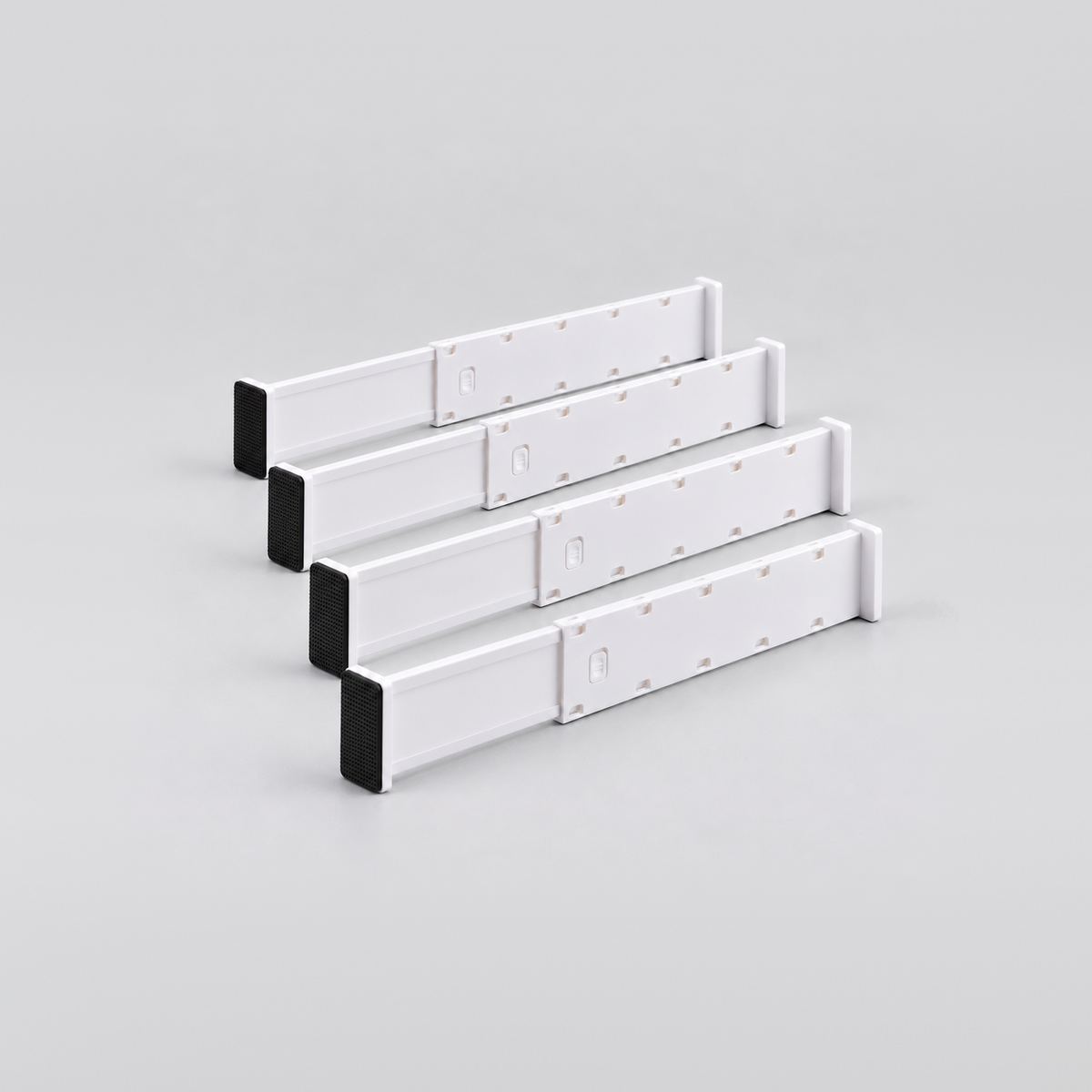 Four short white expandable drawer dividers lined up on a light grey background