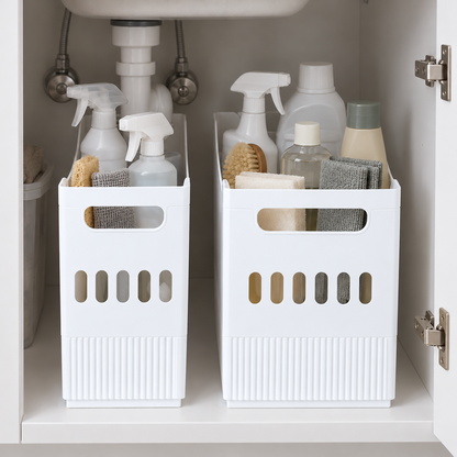 Two white storage bins holding cleaning bottles, sponges and cloths inside an under-sink cabinet