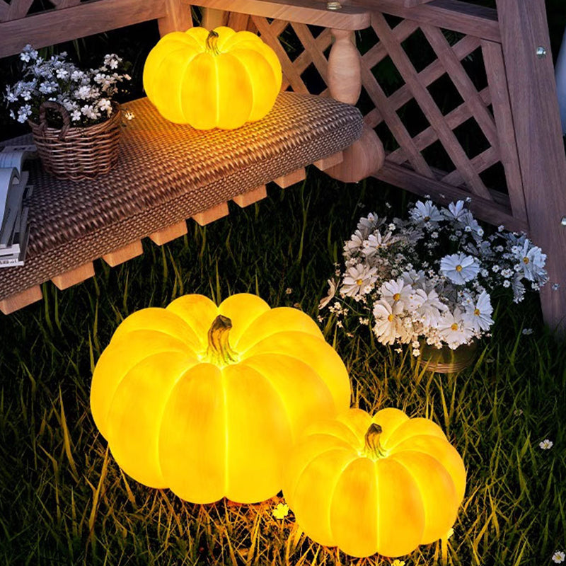 Three glowing resin pumpkin lamps in a garden at night, one on a woven bench and two on the grass among daisies