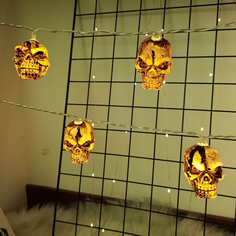 Skull string lights hung in two rows across a wall grid, each small brown skull glowing warm from inside