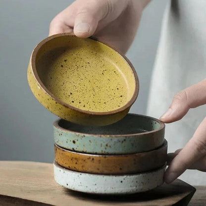 Four speckled ceramic sauce dishes in gray, brown, white and yellow stacked on a wooden board