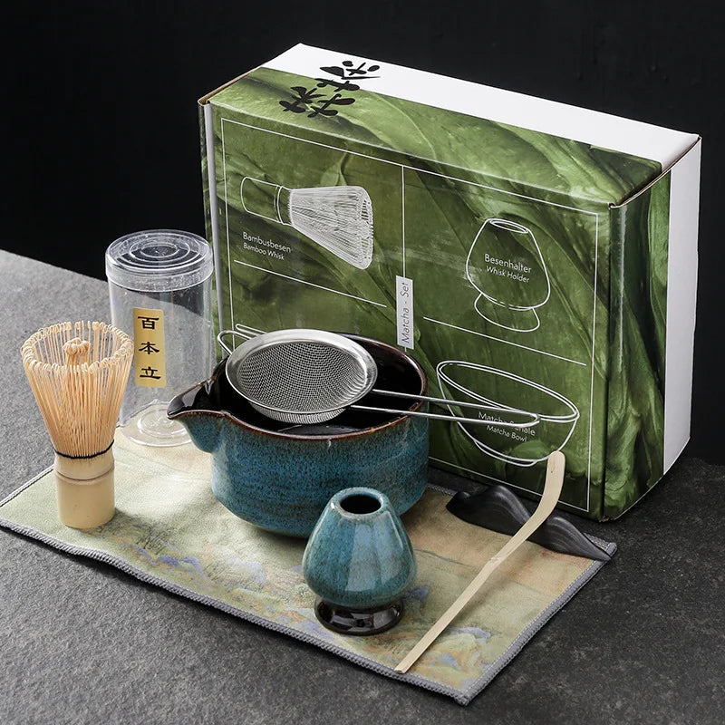 Blue seven-piece matcha kit: spouted ceramic bowl with a steel sifter across it, bamboo whisk, blue whisk holder, bamboo scoop on its rest and a printed cloth; the box behind is not part of the listing