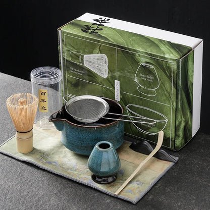 Blue seven-piece matcha kit: spouted ceramic bowl with a steel sifter across it, bamboo whisk, blue whisk holder, bamboo scoop on its rest and a printed cloth; the box behind is not part of the listing