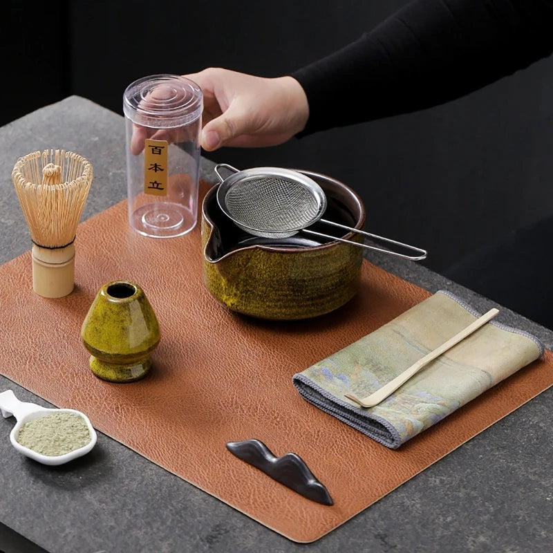 Yellow seven-piece matcha kit laid out: bowl with sifter, whisk, whisk tube, holder, scoop on the printed cloth and the scoop rest; leather mat and white spoon not included
