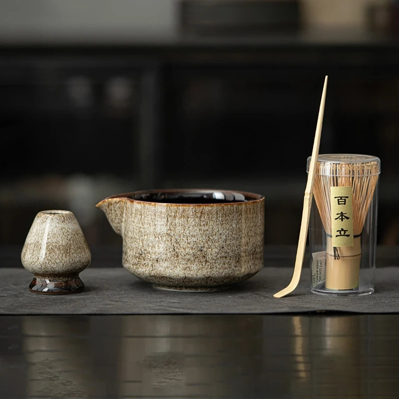 Beige four-piece matcha kit in a row: whisk holder, spouted ceramic bowl, bamboo scoop and bamboo whisk