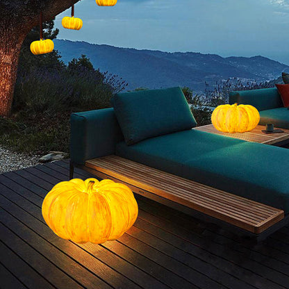 Glowing pumpkin lamps on a terrace at dusk, one on the decking beside a green outdoor sofa and one on a side table
