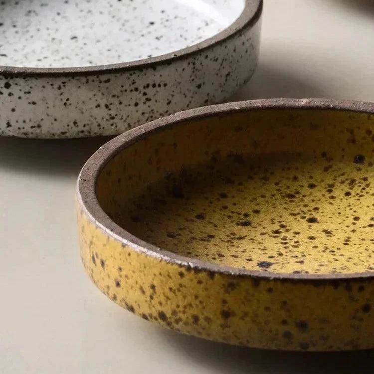 Close view of a white and a yellow speckled ceramic dish showing the straight sides and brown rim