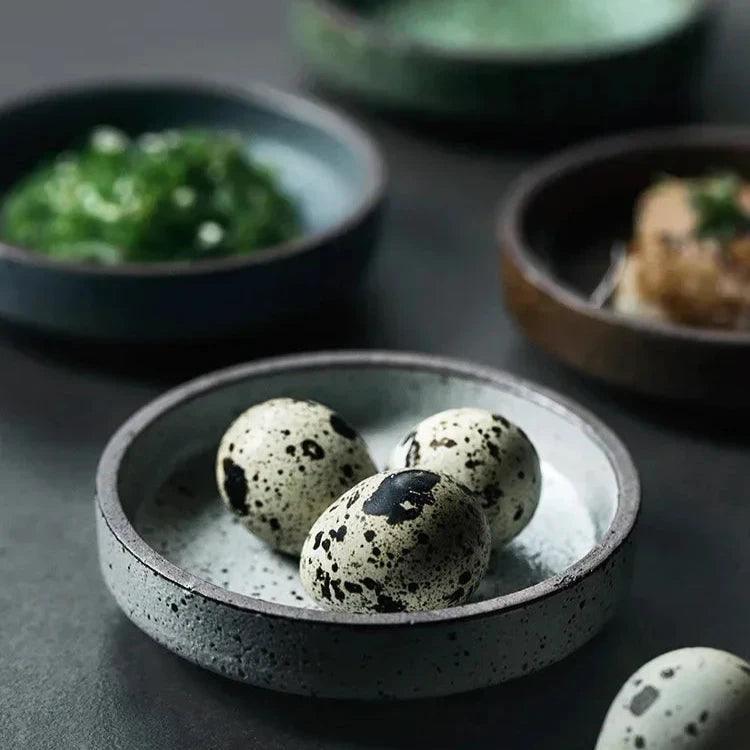 Speckled ceramic dishes on a dark table, the front one holding quail eggs and others holding small side dishes