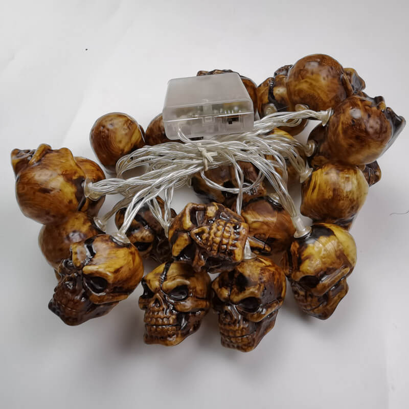 A whole skull string light switched off on white, showing the glossy brown skulls and the clear battery box