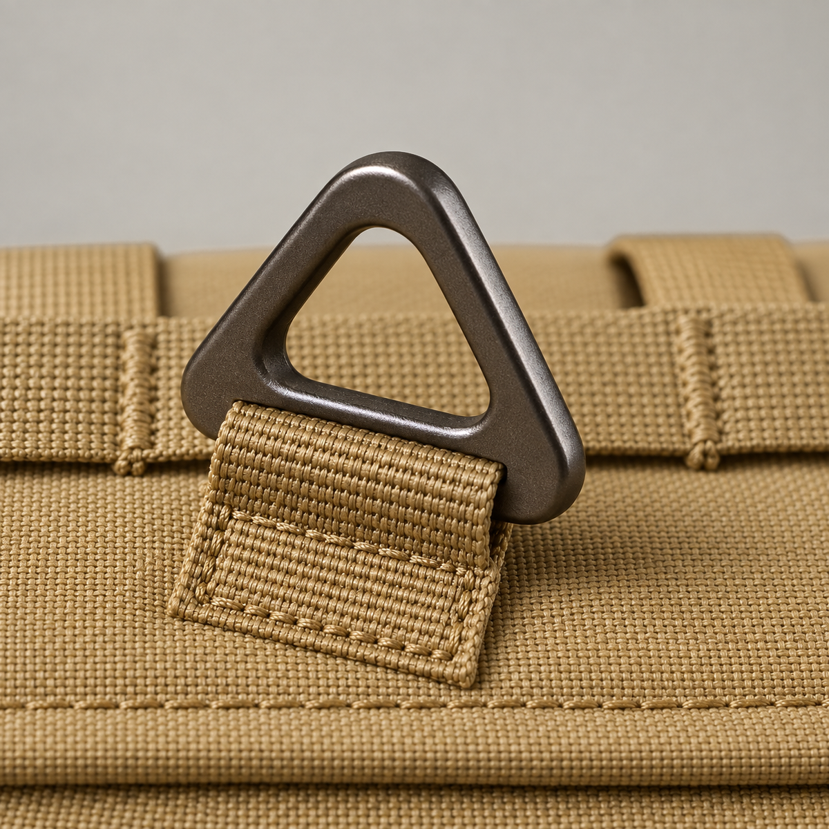 Close up of a triangular metal leash ring on a webbing tab, with rows of tacked webbing on the back panel