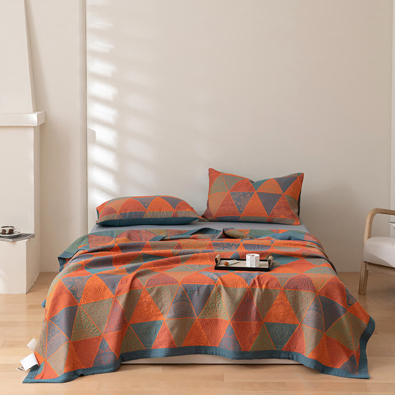 Triangle pattern cotton quilt in orange and slate blue spread over a bed with matching pillowcases